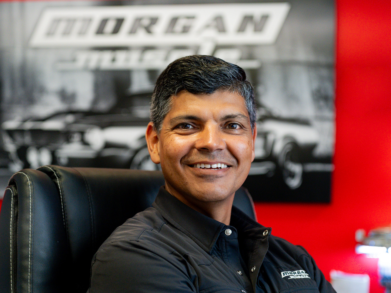 Edgar Barron, shop foreman at Morgan Muscle Cars, smiling in front of the shop's classic car mural in Pelham, Alabama.