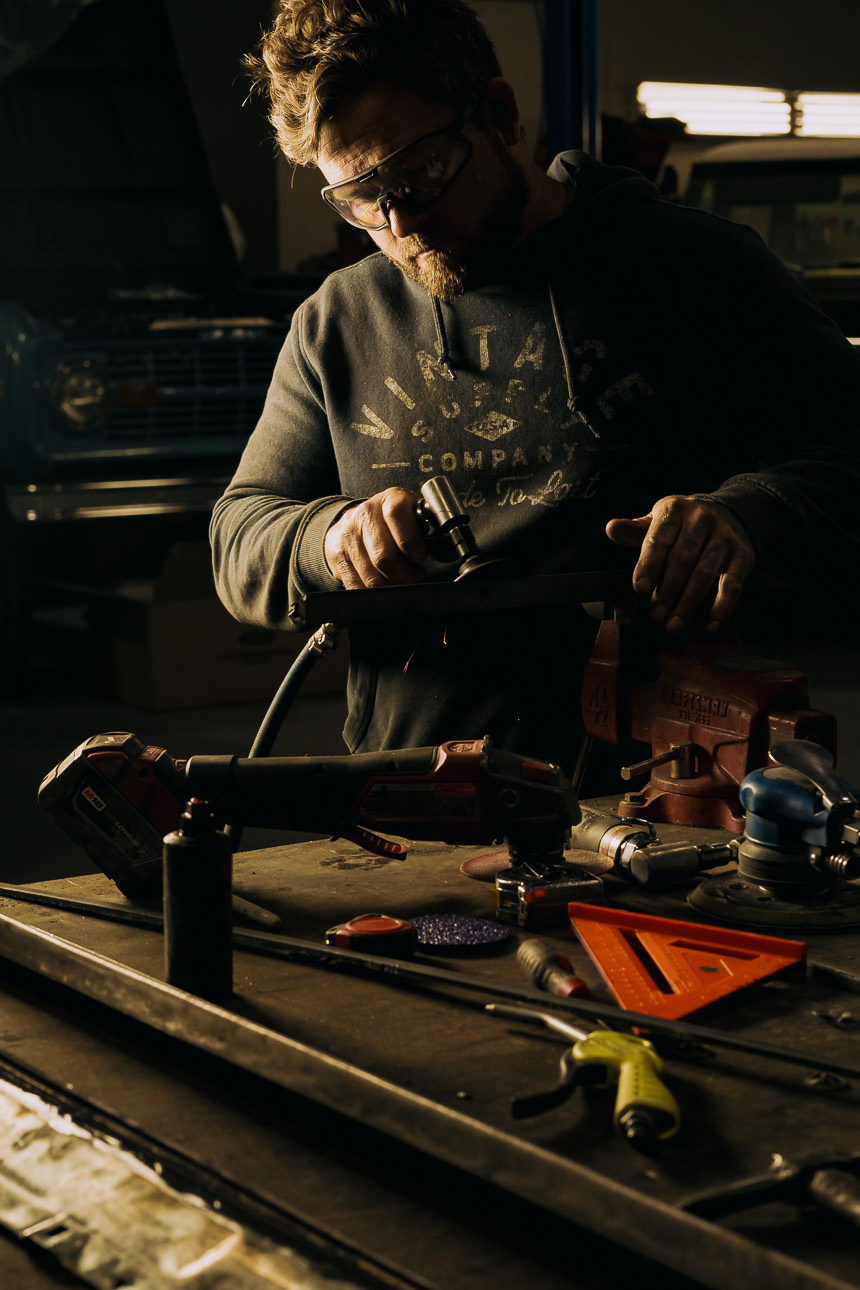 A Morgan Muscle Cars craftsman fabricating a part at the workbench, a classic Ford Bronco in the background, in the Pelham, Alabama shop.